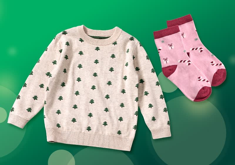 Kinderpullover in Beige mit grünem Tannenbaum‑Allovermuster und ein Paar rosa Socken mit dunkelrotem Bündchen und Zuckerstangenmuster