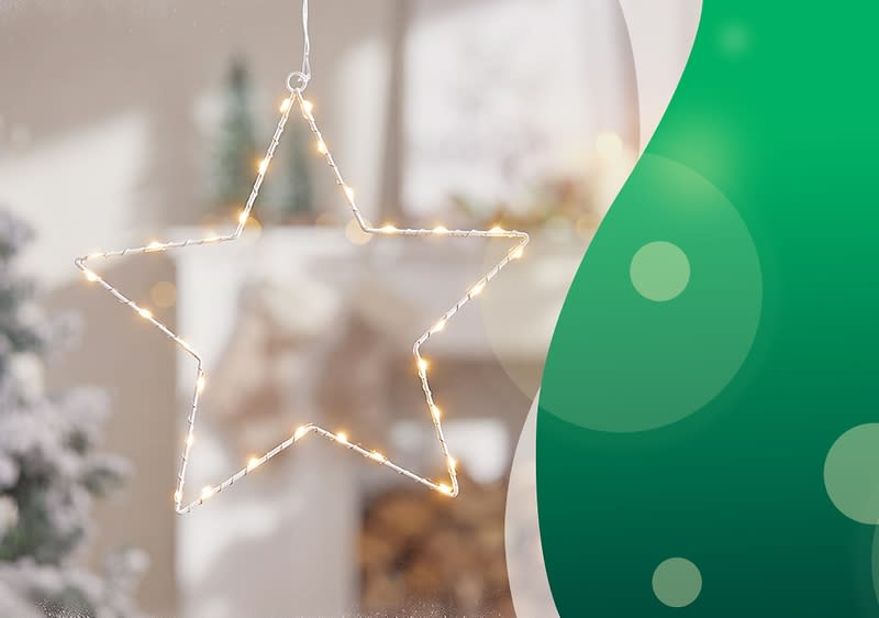 beleuchteter Drahtstern mit warmweißen Lichterketten hängt vor unscharfem Fenster, rechts grüner grafischer Bogen mit hellen Punkten. Bild mithilfe von KI erstellt
