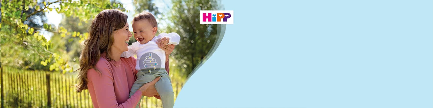 Eine Frau in einem rosa Pullover hält ein Kleinkind in einem weißen Oberteil und grüner Hose im Arm, das Logo von HiPP ist oben rechts im Bild
