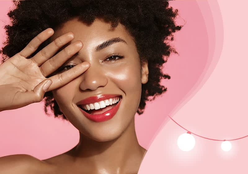 Eine Person mit lockigem Haar hebt die rechte Hand vor einem rosa Hintergrund