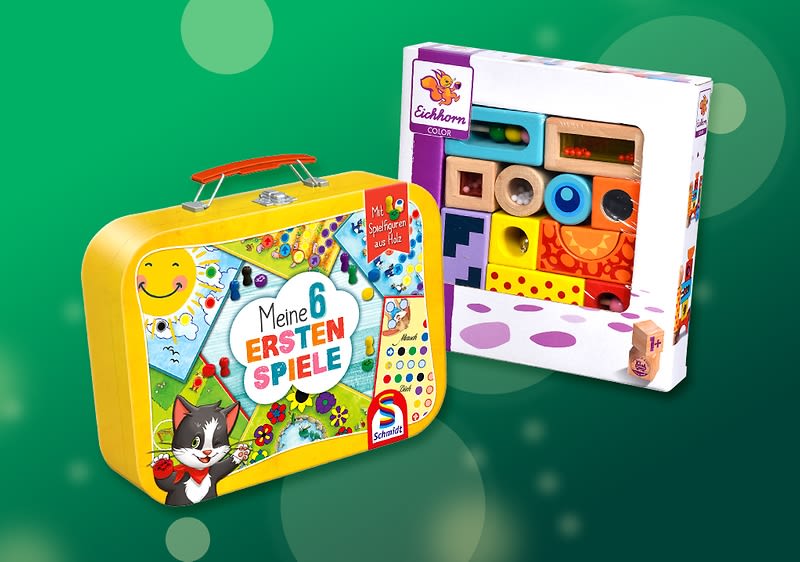 Gelber Spielzeugkoffer mit Aufschrift „Meine 6 ersten Spiele“ und Comic-Katze daneben eine offene Schachtel mit bunten Holzbausteinen und Formen