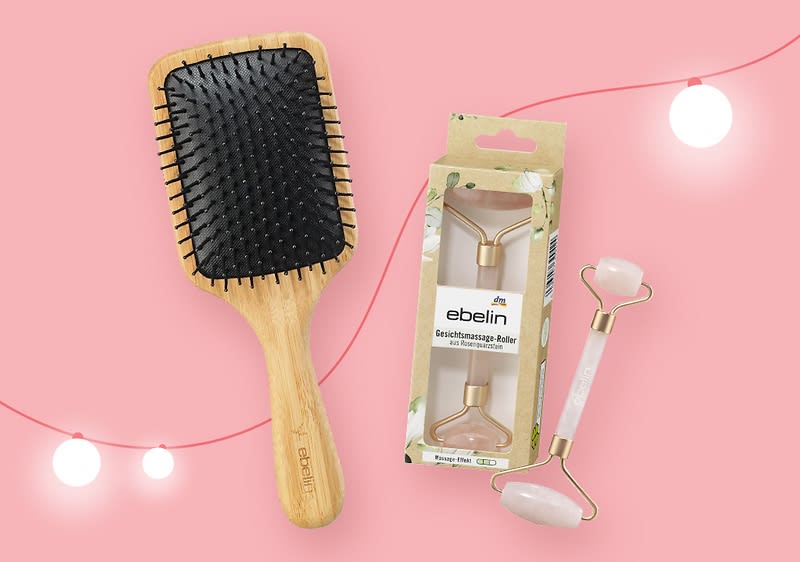 Ein rechteckiger Haarbürste mit Holzgriff und schwarzen Borsten liegt neben einer Verpackung mit einem Gesichtsmassage-Roller von ebelin, der aus rosa und weißem Stein besteht