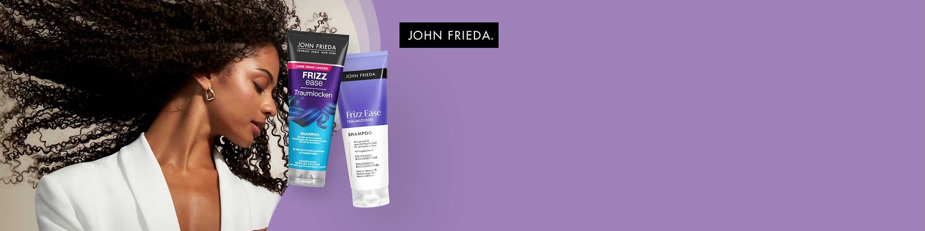 Zwei Shampoo-Flaschen der Marke John Frieda auf lila Hintergrund. Links eine Flasche mit der Aufschrift „Frizz Ease Traumlocken“ in Blau und Lila, rechts eine Flasche mit der Aufschrift „Frizz Ease Traumlocken“ in Weiß und Lila. Oben rechts das Logo von John Frieda