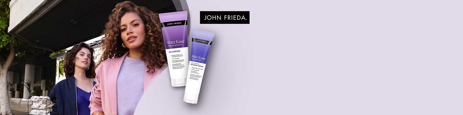 Zwei John Frieda Produkte: Eine lila Shampoo-Flasche mit der Aufschrift „Frizz Ease Shampoo“ und eine lila Tube mit der Aufschrift „Frizz Ease Locken Creme“. Oben rechts das Logo von John Frieda