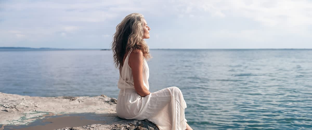 Žena u zrelijim godinama na plaži gleda u more