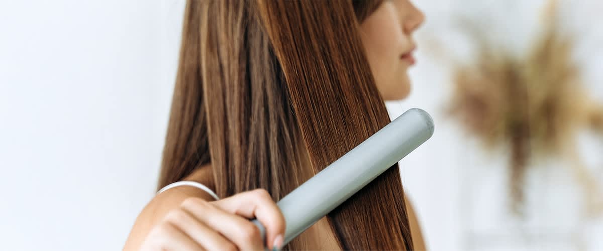 Ravnanje kose peglom za kosu na dugoj smeđoj kosi