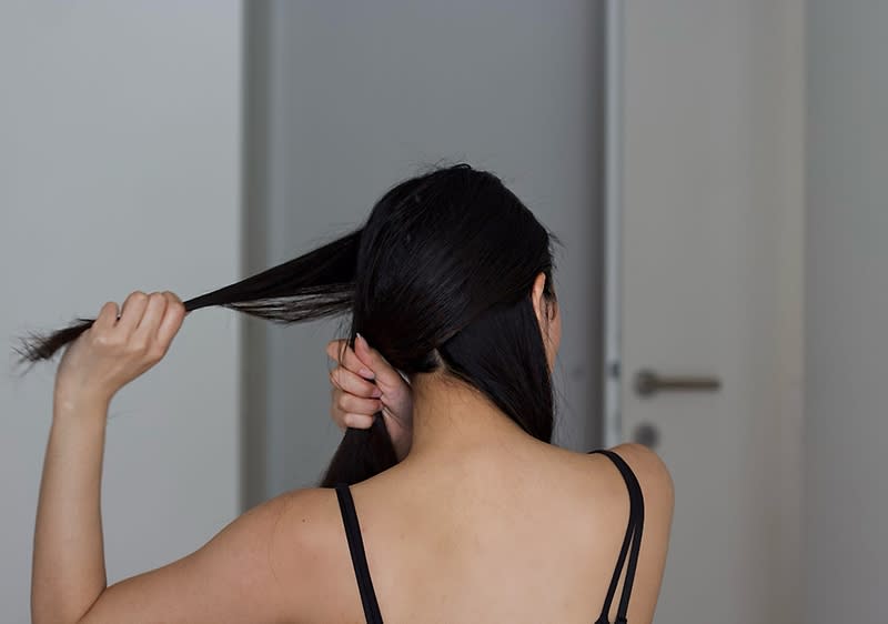 Žena veže svoju dugu crnu kosu u pletenicu na suprotnoj strani