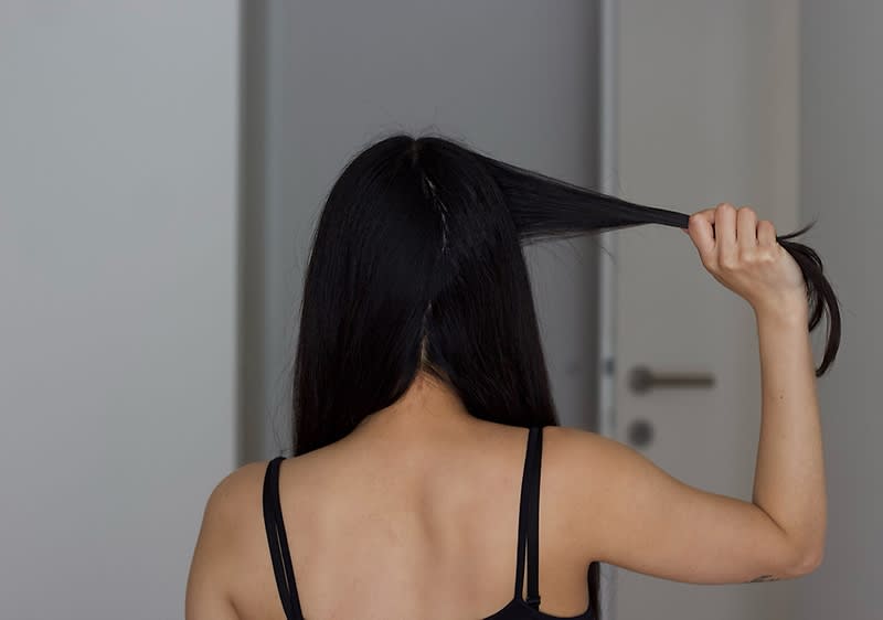Žena veže svoju dugu crnu kosu u pletenicu