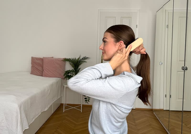 Žena češlja kosu unatrag u spavaćoj sobi s krevetom i biljkama