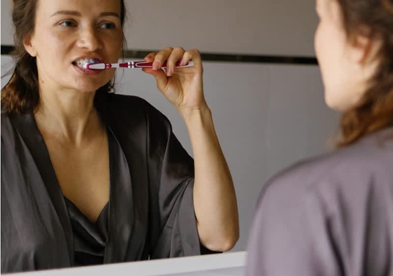 Djevojka pere zube pred ogledalom u kupaonici