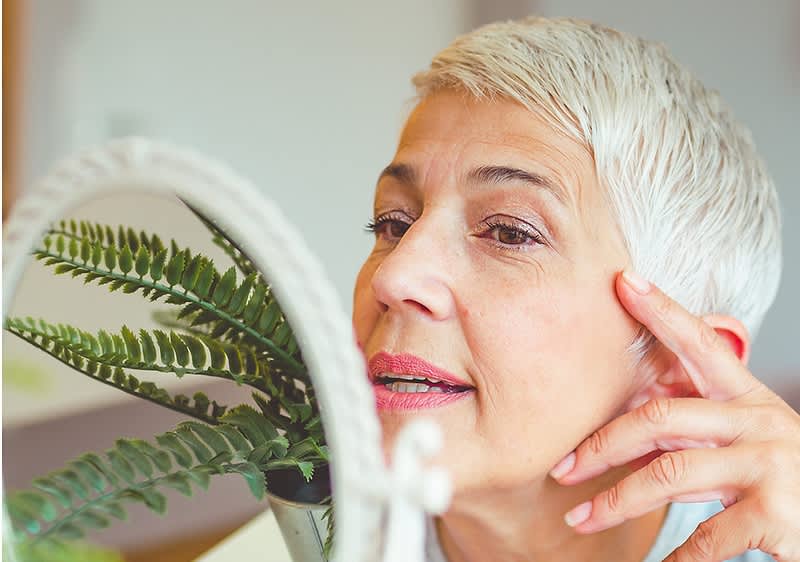 Žena zrele dobi proučava svoje lice u ogledalu