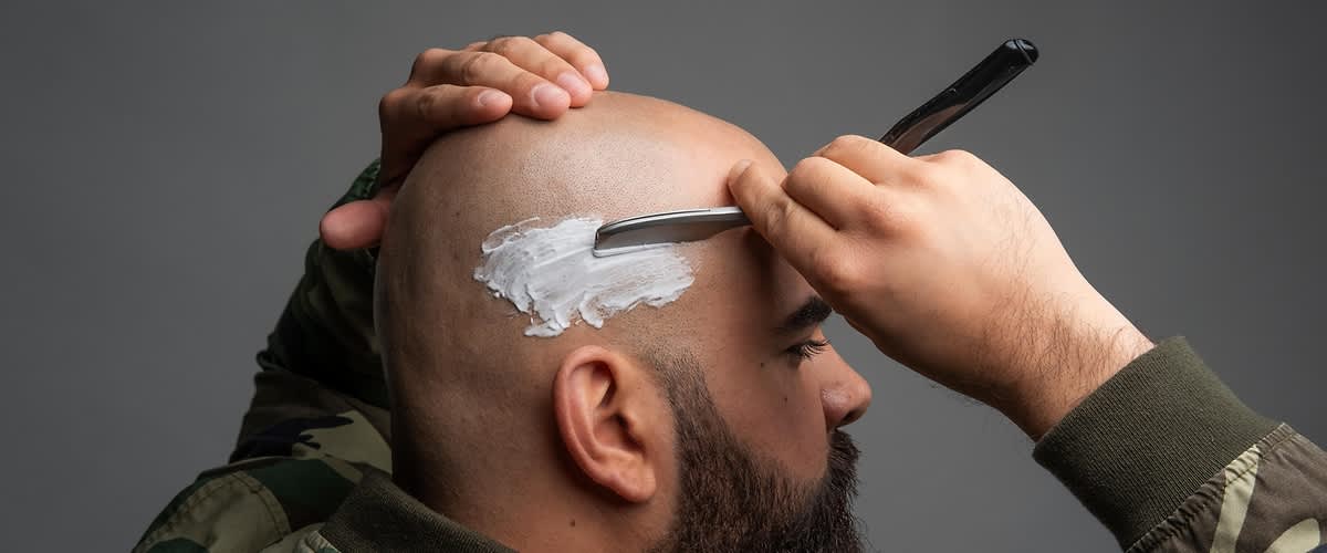 Muškarac s gustom bradom brije glavu brijačem