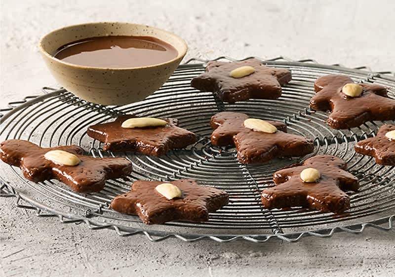 Osam medenjaka u obliku zvijezde s bademima na okrugloj rešetki, pored zdjele čokoladnog umaka