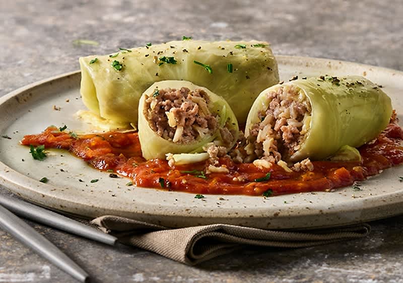 Dvije veganske rolade od kupusa na tanjuru s umakom od rajčice, ukrašene svježim začinskim biljem