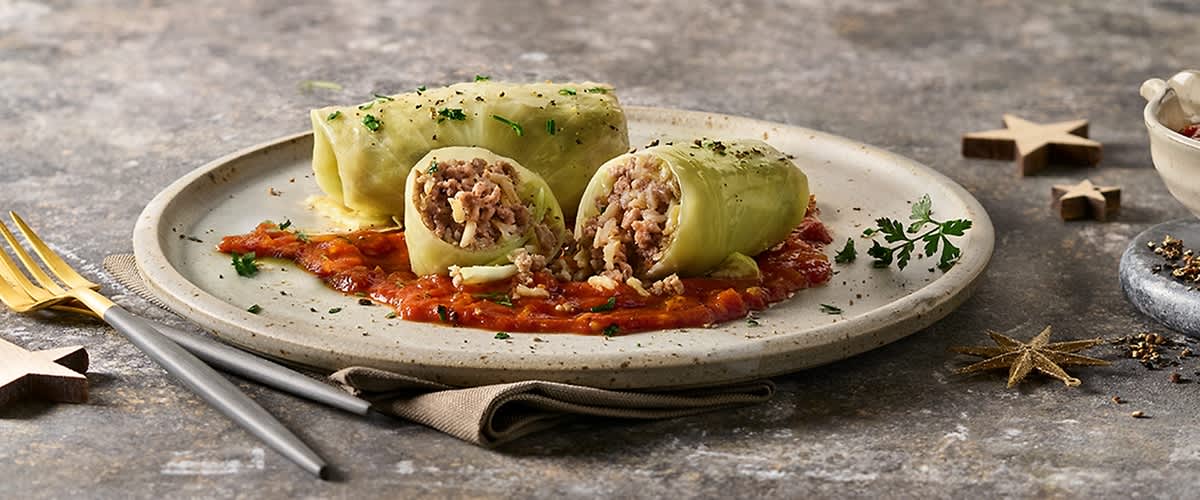 Dvije veganske rolade od kupusa na tanjuru s umakom od rajčice, ukrašene svježim začinskim biljem