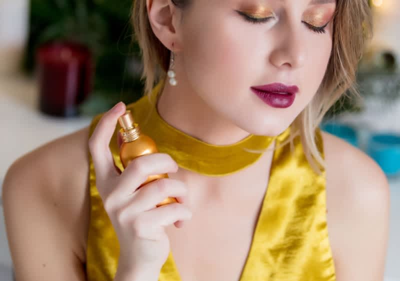djevojka u žutoj haljini nanosi parfem na vrat