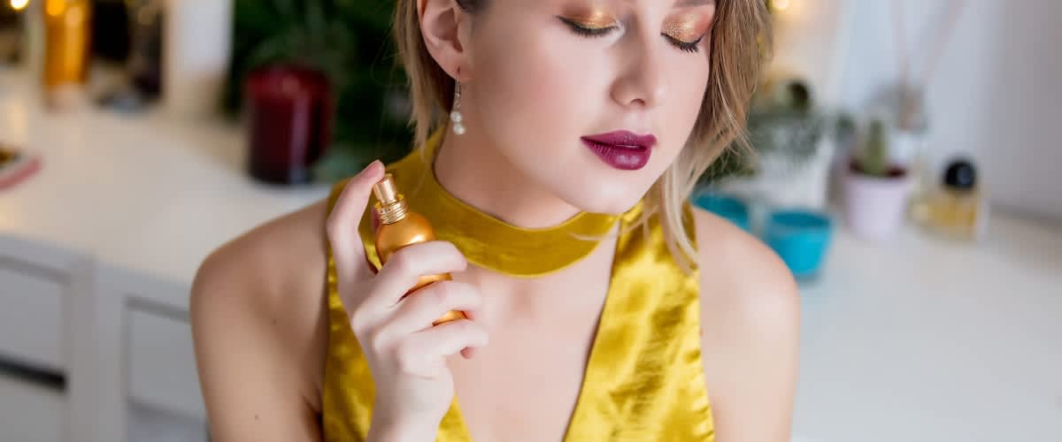 djevojka u žutoj haljini nanosi parfem na vrat