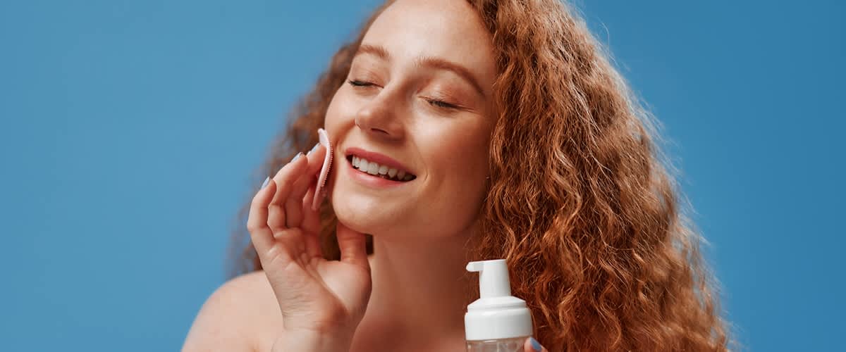 djevojka duge kovrčave crvene kose čisti lice blazinicom