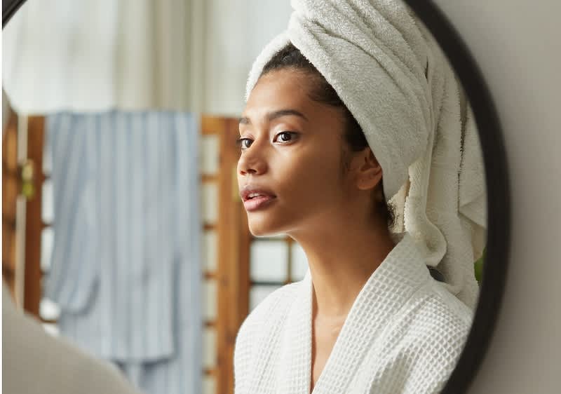 Djevojka s ručnikom u kosi se promatra u ogladalu