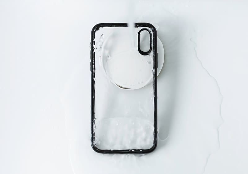 Crna maskica za pametni telefon leži na bijeloj pozadini i polijevaju je vodom.