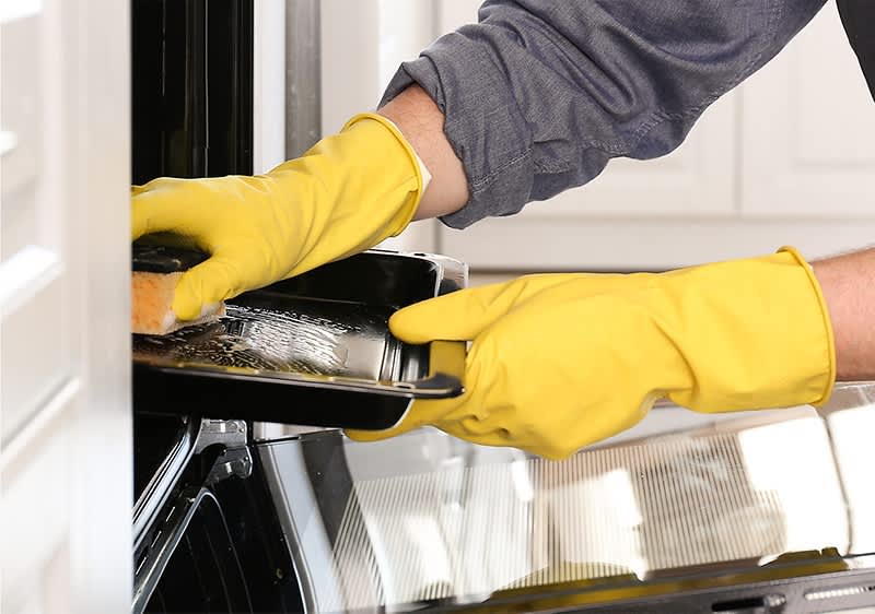 Dvije ruke u žutim zaštitnim rikavicama čiste tepsiju