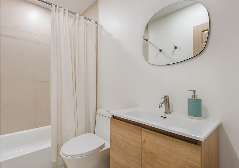 Moderna kupaonica s bijelom kadom, bež zavjesom za tuširanje, bijelim umivaonikom i ovalnim ogledalom.dernes Badezimmer mit einer weißen Badewanne, einem beigen Duschvorhang, einem weißen Waschbecken und einem ovalen Spiegel.