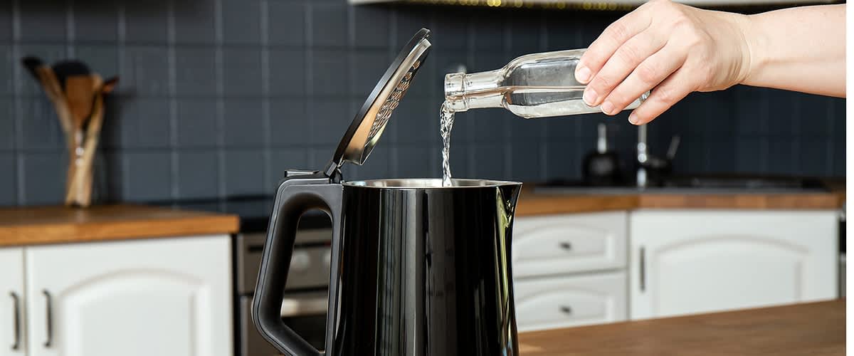 Voda se iz staklene boce ulijeva u otvoreno crno kuhalo za vodu