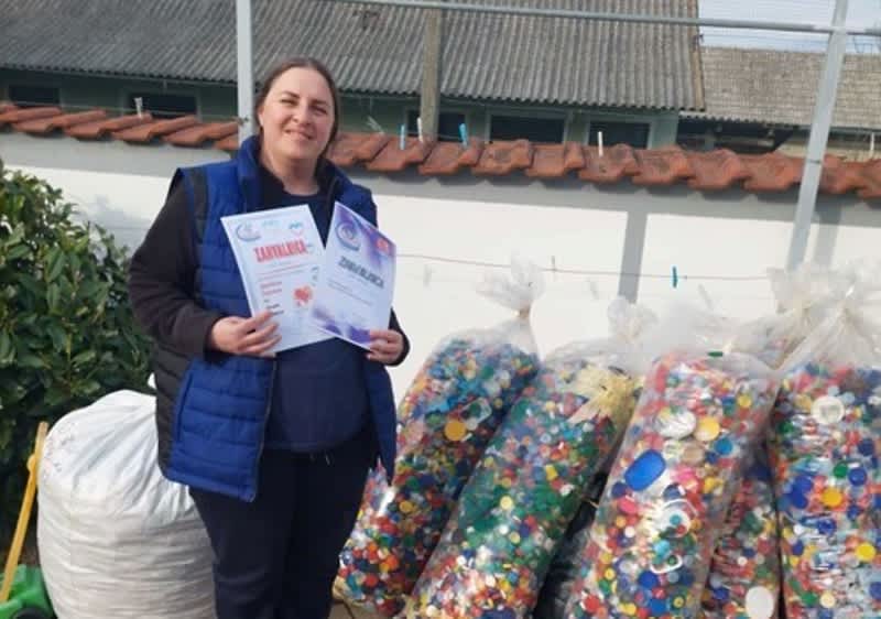 Ivana drži u ruci dvije zahvalnice iza nje u pozadini vreće s plastičnim čepovima