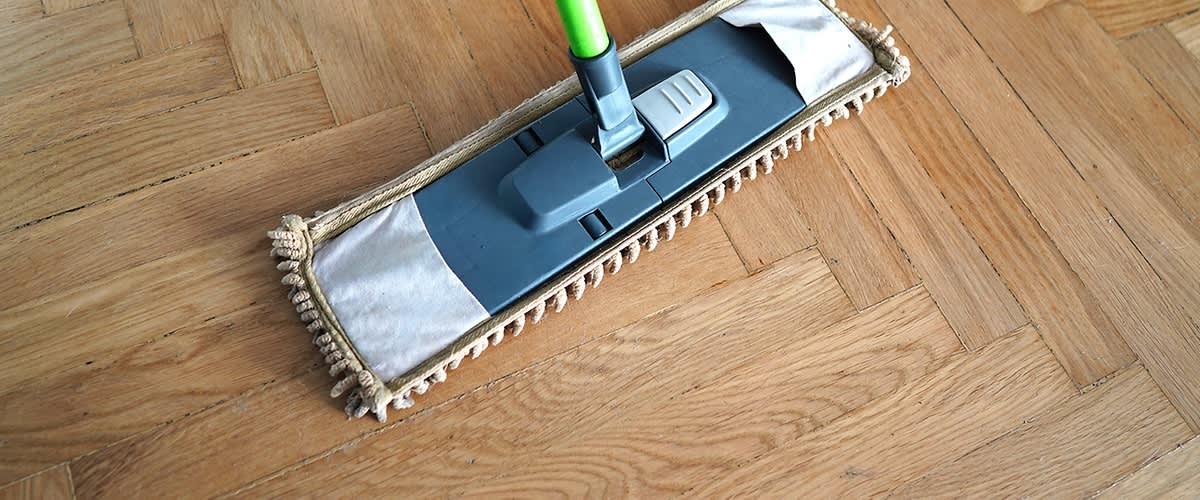 Mop sa sivomkrpom od mikrovlakana i zelenom drškom čisti drveni pod s uzorkom riblje kosti