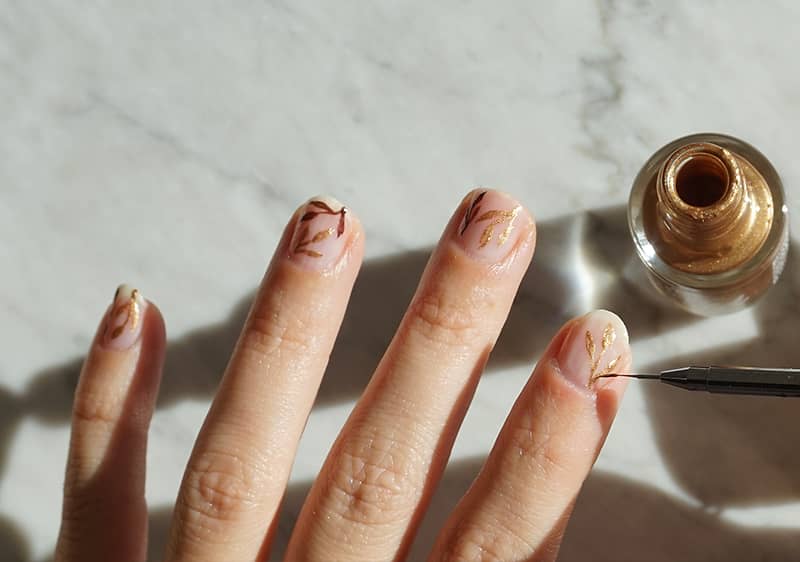 Ruka s pet kratko isturpijanih noktiju, svijetlo nude bazom i finim zlatnim linijama kao nail artom
