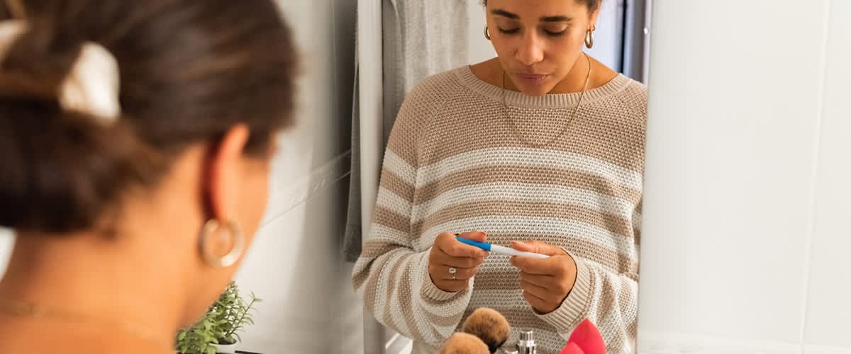 Slika žene u kupaonici koja drži i gleda test trudnoće