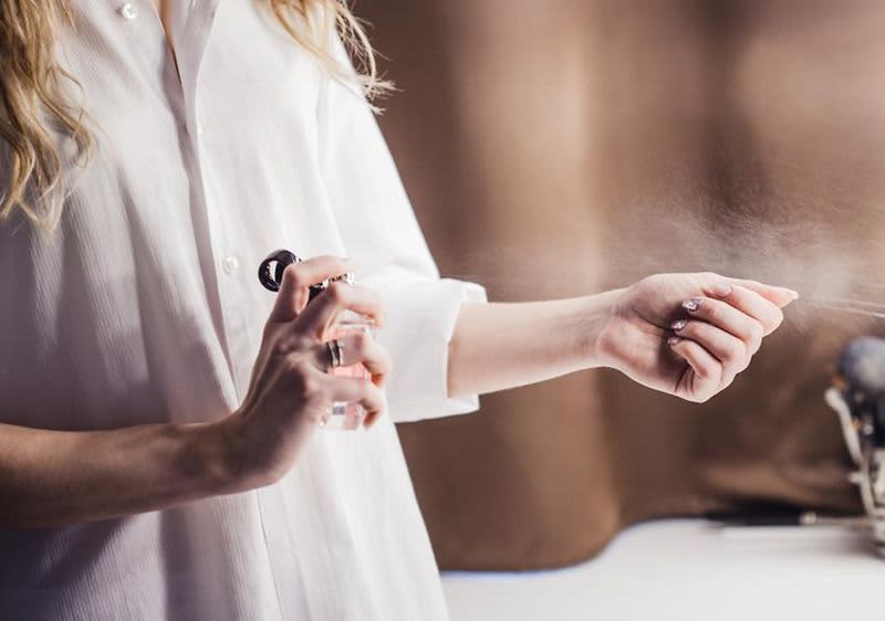 žena u bijeloj košulji koja testira miris na svoj ruci