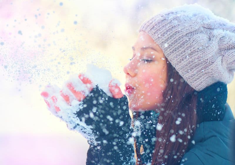 djevojka koja puše u grudu snijega koju drži u rukama