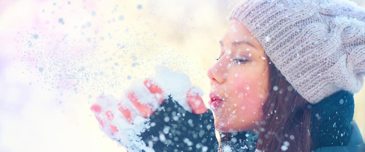 djevojka koja puše u grudu snijega koju drži u rukama