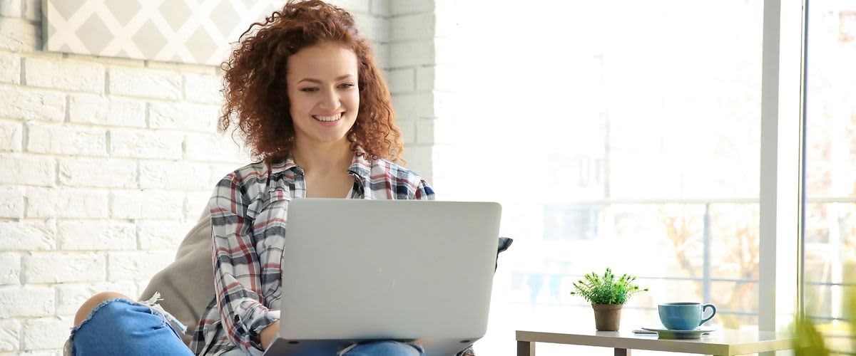 žena koja sjedi kod kuće u fotelji i radi na prijenosnom računalu