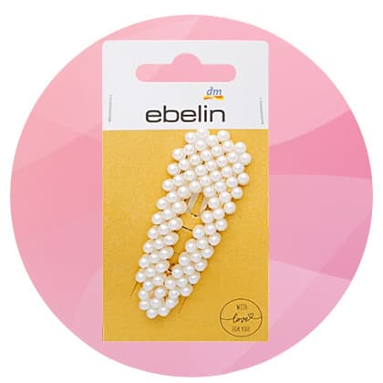 Eine silberne Flasche Balea Glow Perfect Shine Coat neben einer weißen invisibobble Clipstar Haarspange auf rosa Hintergrund
