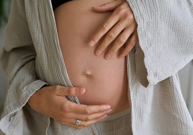 Kismama keze a pocakján, szürke köntösben, gyűrűt viselve