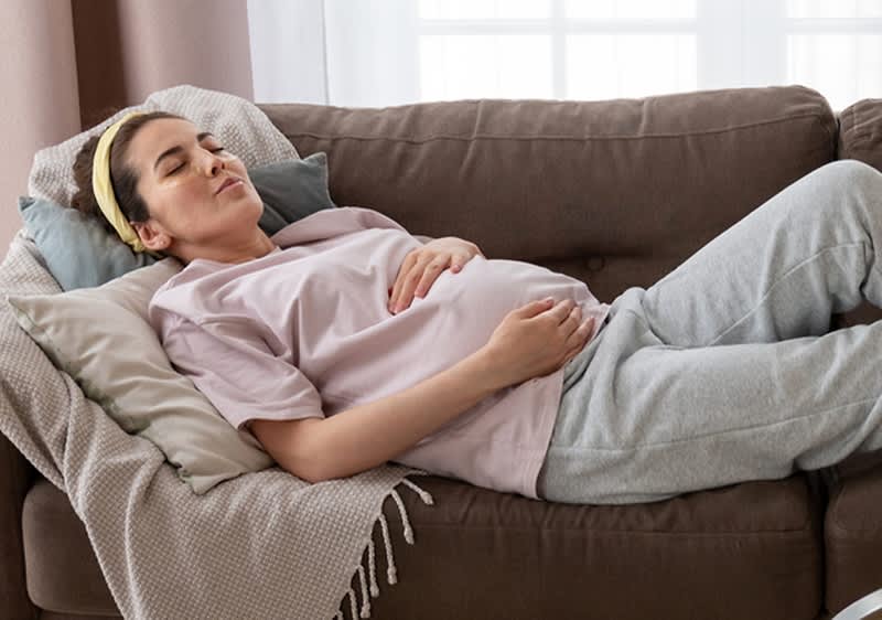 Várandós nő melegítőruhában fekszik egy kanapén