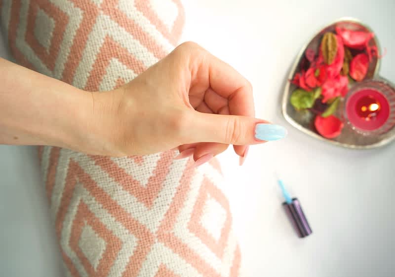 Manikűr: Kék körömlakkos kéz, rózsaszín mintás párna, szív alakú tálcán virágok és gyertya