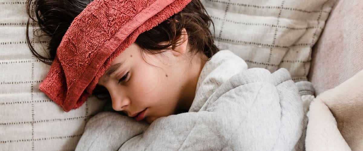 Beteg kisgyerek egy vizes ruhával a homlokán fekszik az ágyban