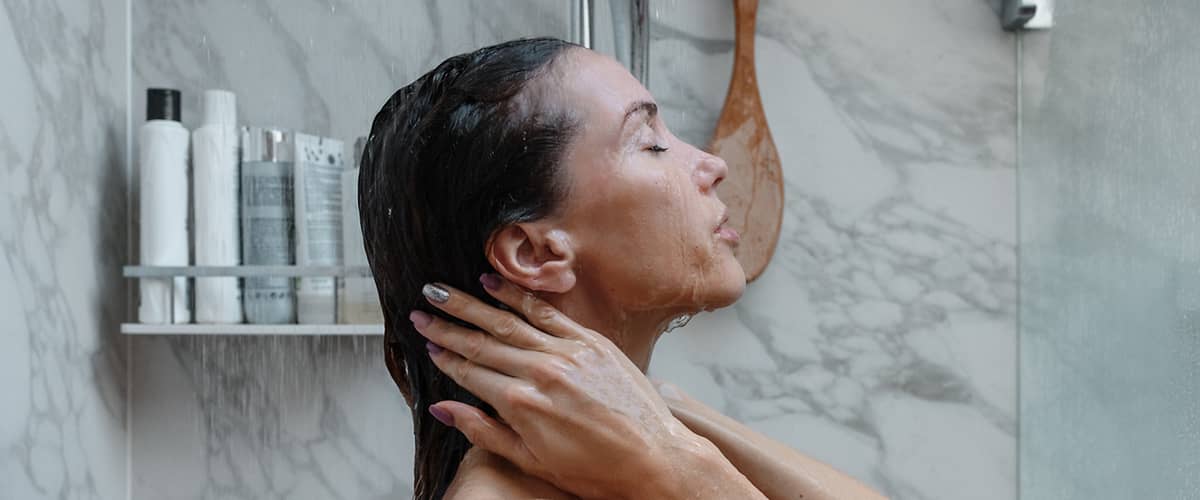 Frau unter Dusche mit Shampoo-Flaschen im Hintergrund