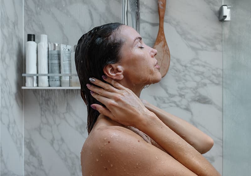 Frau beim Duschen mit Shampoo-Flaschen im Hintergrund