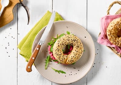 Bagel szendvics tányéron kés és zöld szalvéta mellett