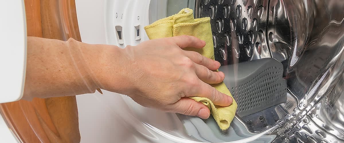 Kéz töröl egy mosógépet egy sárga ronggyal.