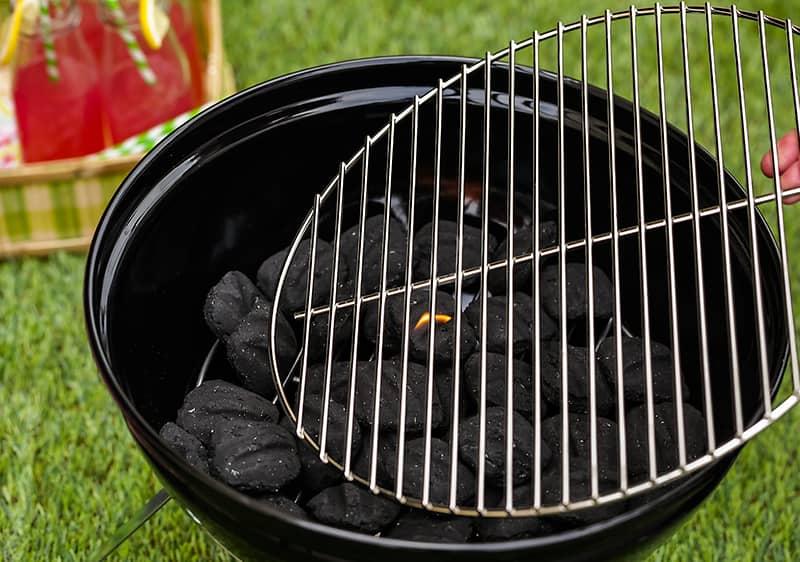 Grill szénnel és rácssal készen a sütéshez, zöld fű háttérben
