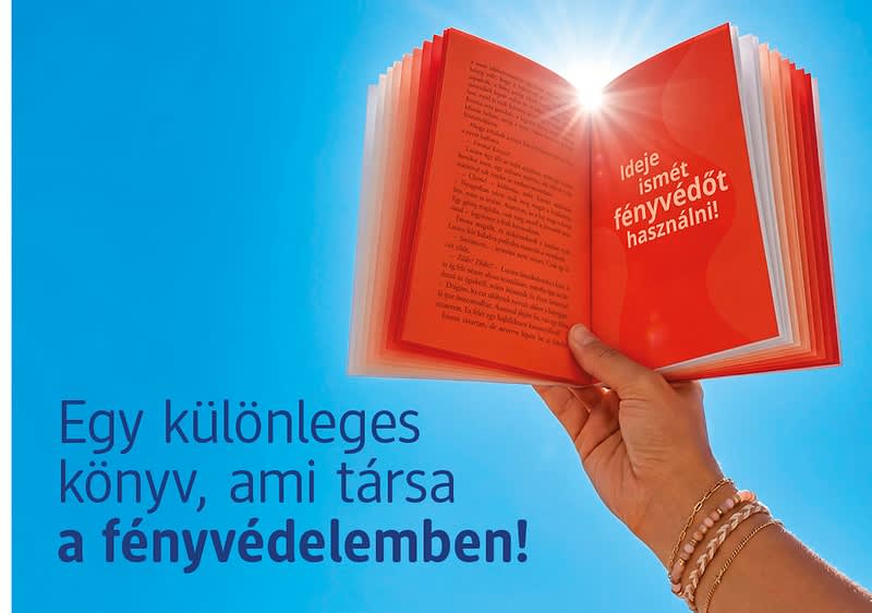 Közeli kép egy kézben tartott, kinyitott piros könyvről, melyből fény sugárzik, kék háttérrel és magyar szöveggel</p>