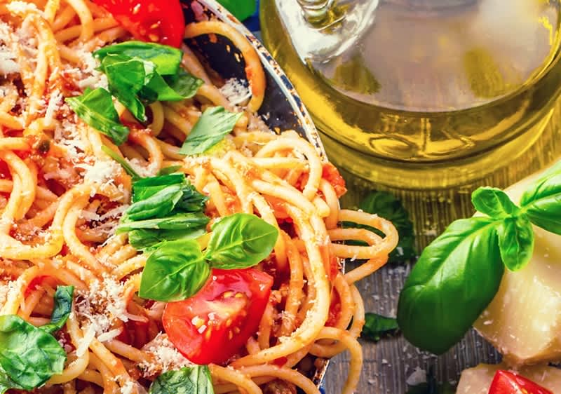 Spagetti paradicsomszósszal, friss bazsalikommal és parmezánnal közelről, olívaolajjal és sajt darabokkal a háttérben