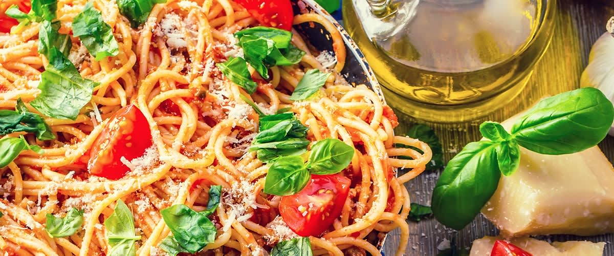 Spagetti paradicsomszósszal, friss bazsalikommal és parmezánnal közelről, olívaolajjal és sajt darabokkal a háttérben