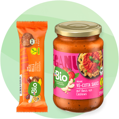 Prodotti della linea limited edition Veganuary a marchio dmBio: energy balls al mango  frutta secca e sugo vegano alla ricotta su sfondo verde sfumato.