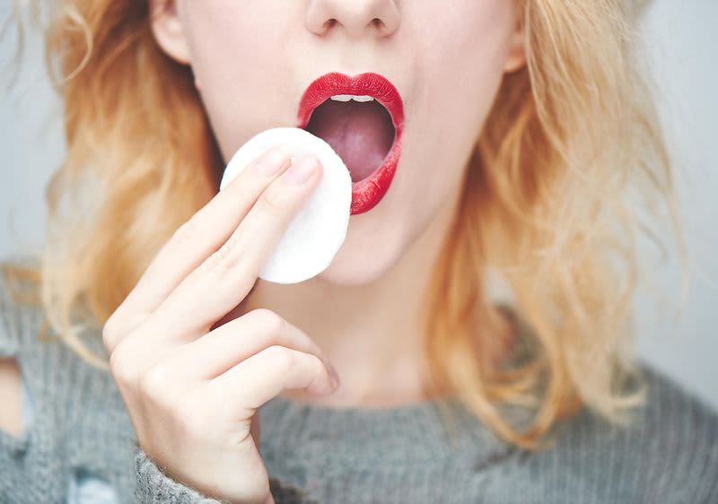 Frau schminkt sich roten Lippenstift ab.